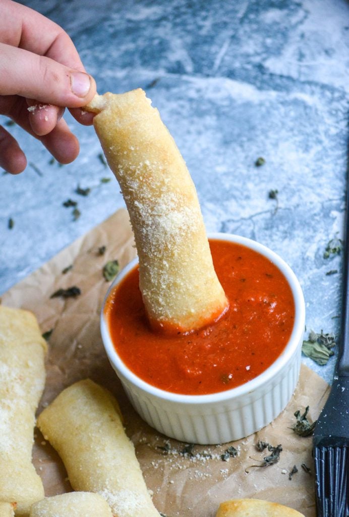 a piece of copy cat little caesar's crazy bread being dipped into a white bowl of bright read marinara sauce