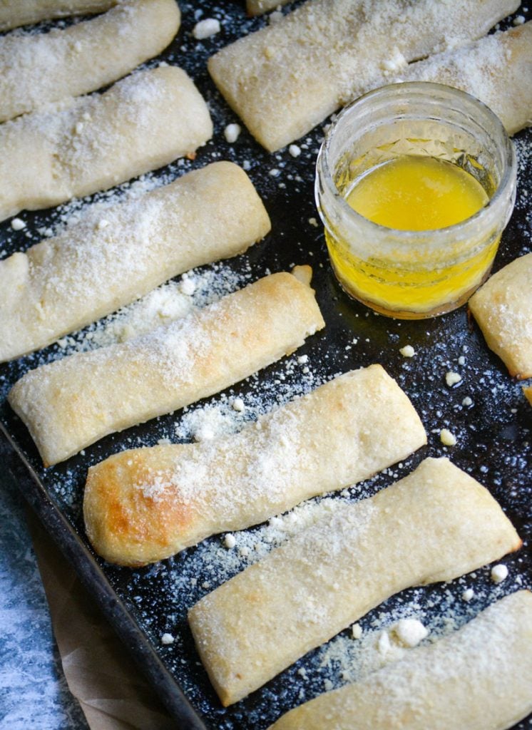 copy cat crazy bread sticks arranged on a baking sheet with melted butter and a silicone brush for spreading