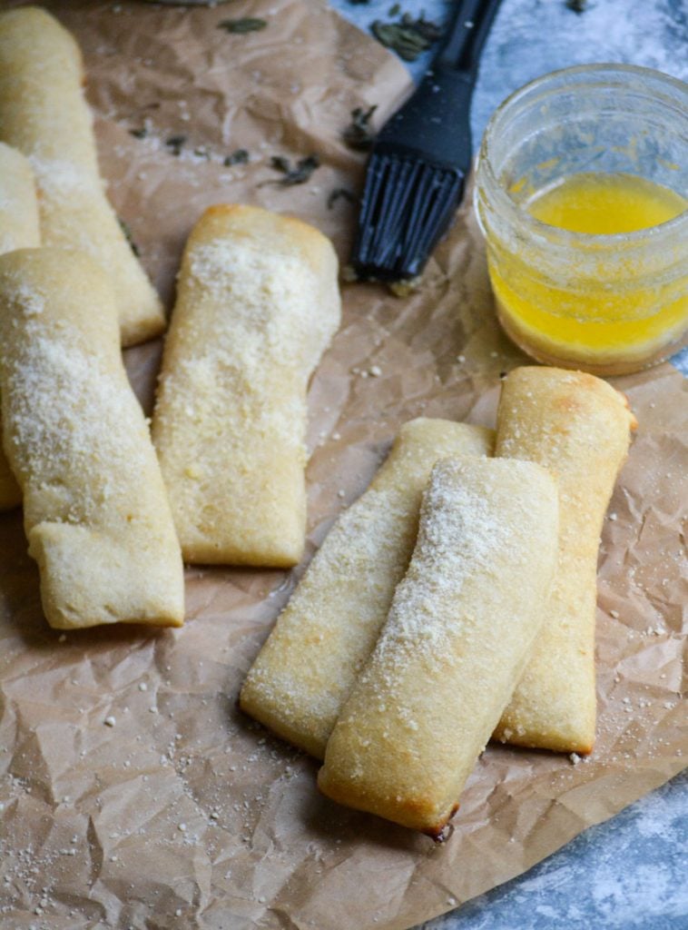 copy cat crazy bread sticks arranged on a baking sheet with melted butter and a silicone brush for spreading