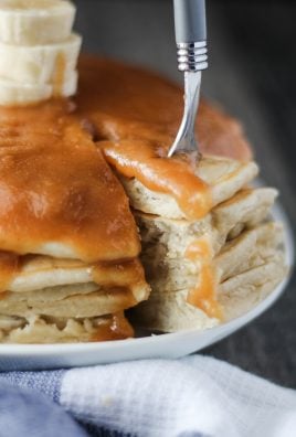 a fork removing a slice of stacked banana pancakes with peanut butter syrup
