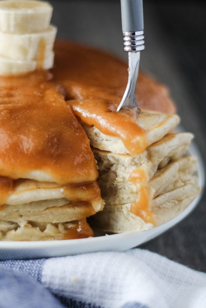 a fork removing a slice of stacked banana pancakes with peanut butter syrup