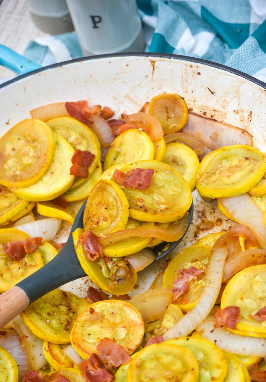 a spoon scooping sauteed summer squash out of a blue skillet
