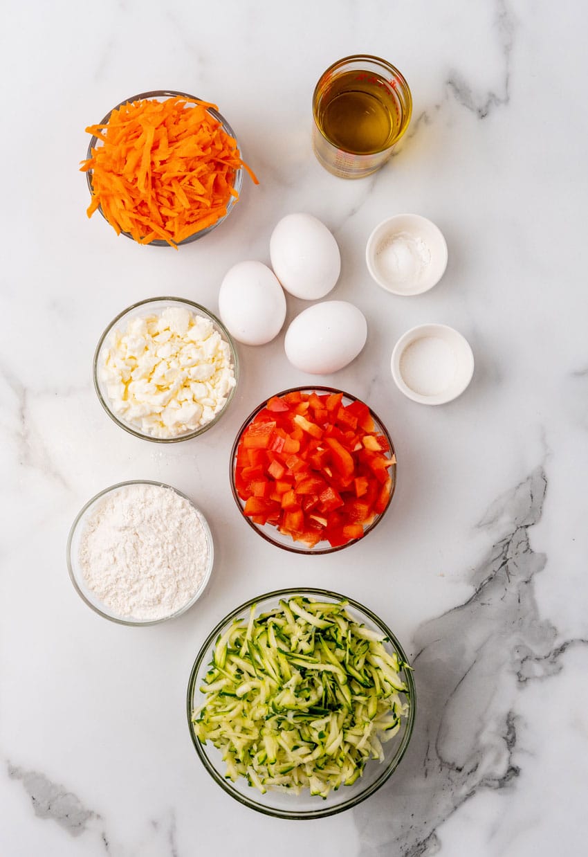 an overhead image showing the measured ingredients needed to make a batch of carrot and zucchini fritters with feta