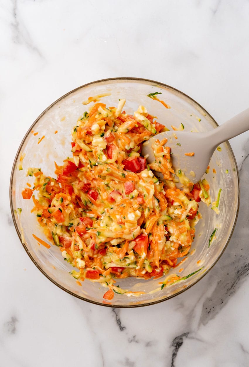 shredded zucchini and carrot mixed with beaten eggs in a glass mixing bowl