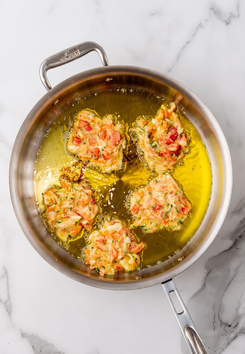 carrot and zucchini fritters with feta frying in a pot of hot oil