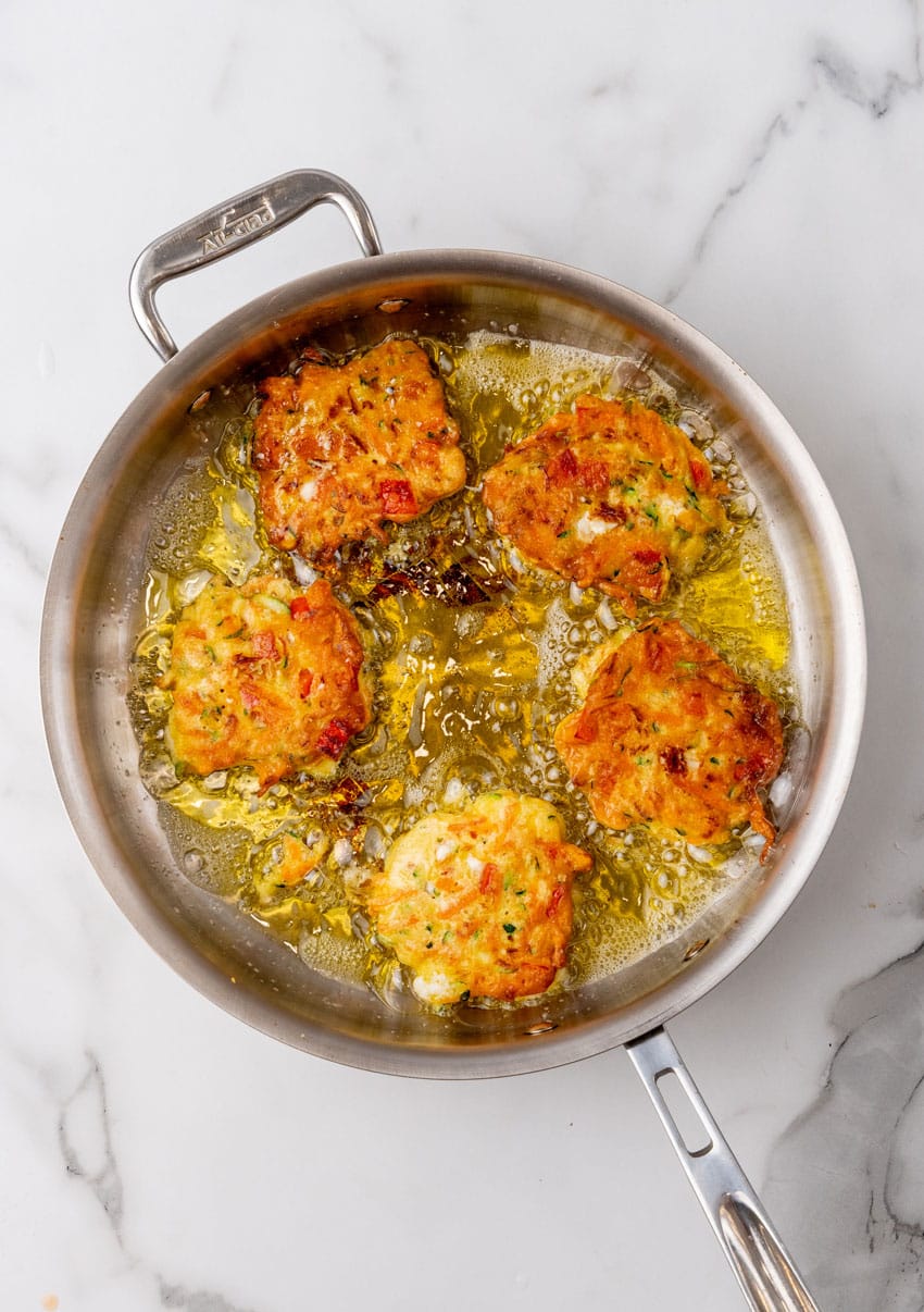 carrot and zucchini fritters with feta frying in a pot of hot oil