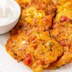 carrot and zucchini fritters with feta piled on a white serving platter with a small bowl of plain yogurt on the side