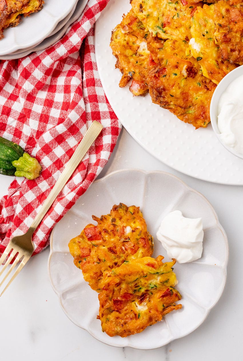 two carrot and zucchini fritters with feta on a small white plate with plain yogurt on the side for dipping