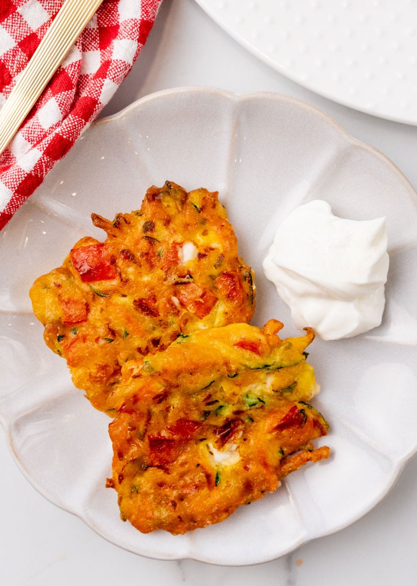 two carrot and zucchini fritters with feta on a small white plate with plain yogurt on the side for dipping