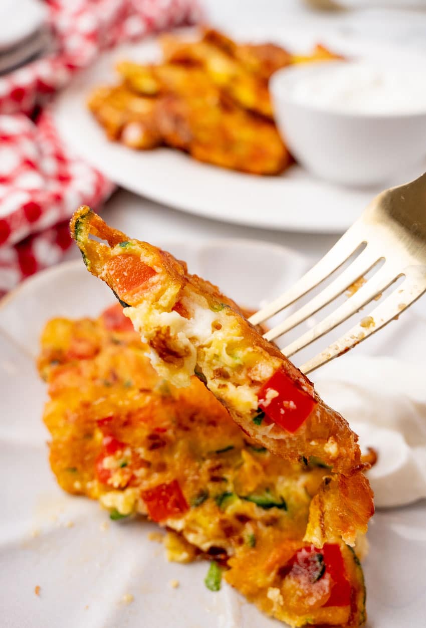 a golden fork holding up a half of a zucchini fritter to reveal the inside