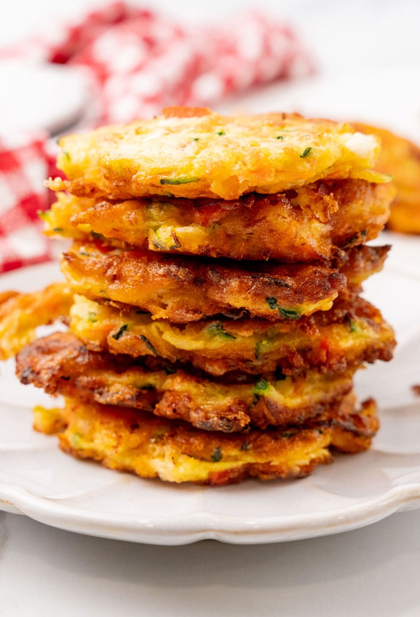 a stack of carrot and zucchini fritters with feta on a small white plate