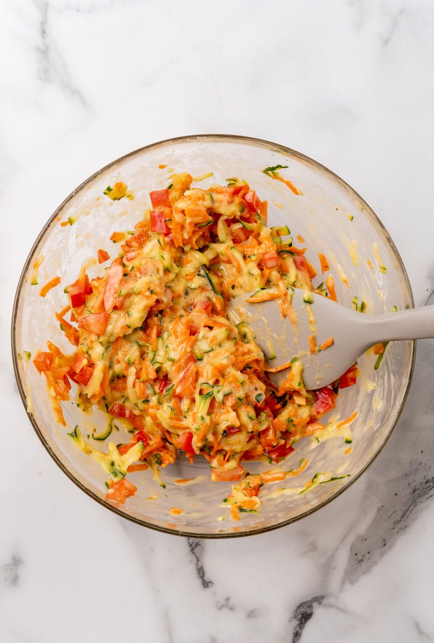 shredded zucchini and carrot mixed with beaten eggs in a glass mixing bowl