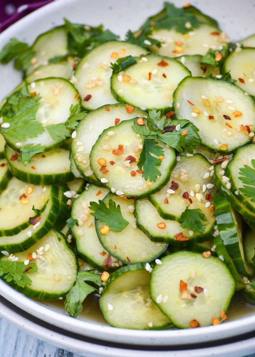 Asian cucumber salad in a white bowl topped with fresh cilantro leaves
