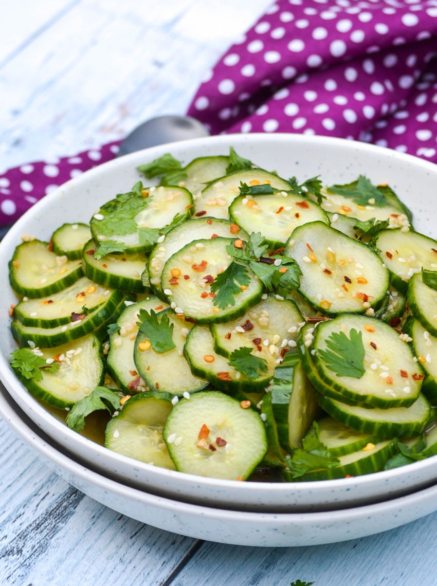 Asian cucumber salad in a white bowl topped with fresh cilantro leaves