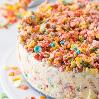 fruity pebble ice cream cake on a white serving tray surrounded by colorful breakfast cereal pieces