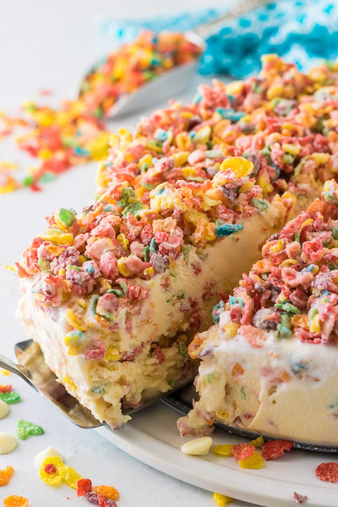 a creamy slice of Fruity Pebble Ice Cream Cake being removed from a springform pan base with a metal cake server