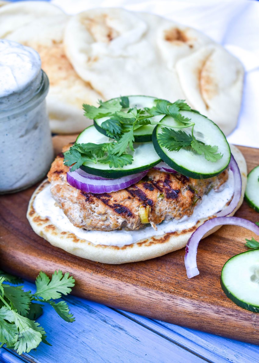 grilled tandoori chicken burgers on naan bread on a wooden cutting board