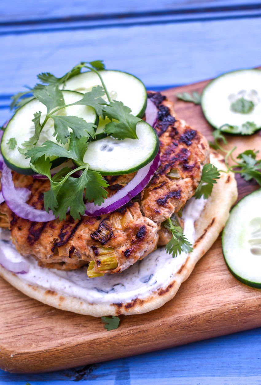 grilled tandoori chicken burgers on naan bread on a wooden cutting board