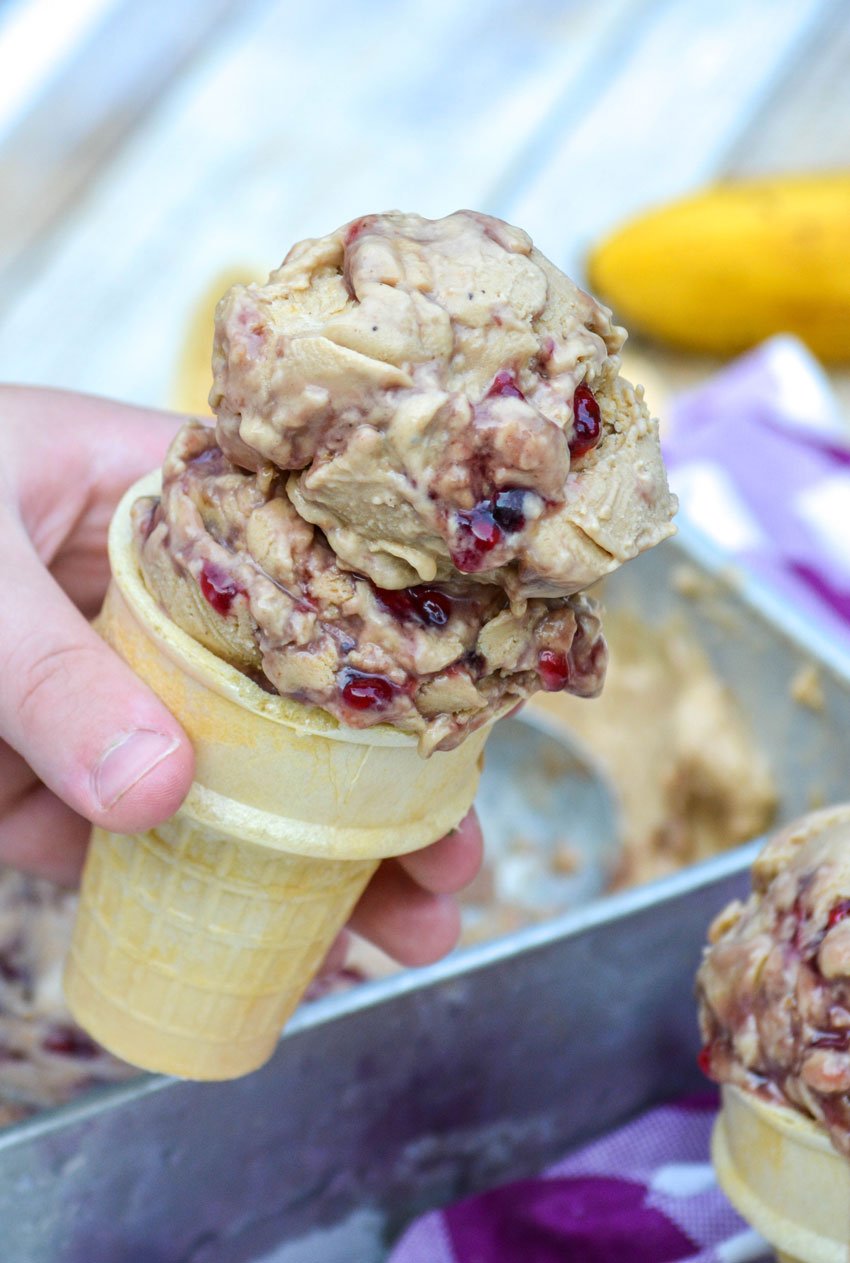 a hand holding up a sugar cone filled with peanut butter and jelly banana nice cream