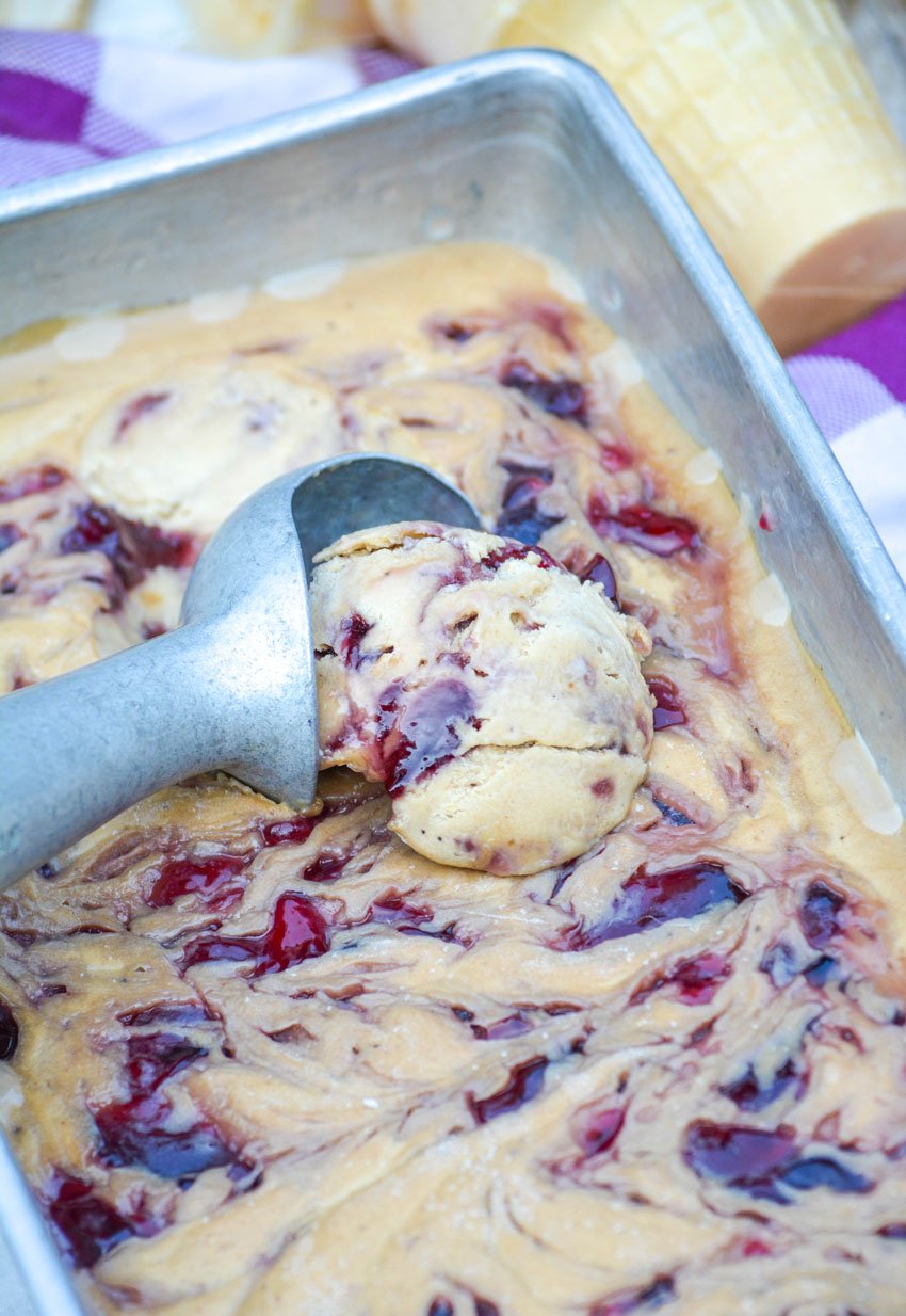 3 ingredient peanut butter and jelly ice cream being scooped by a silver ice cream scoop from a metal loaf pan