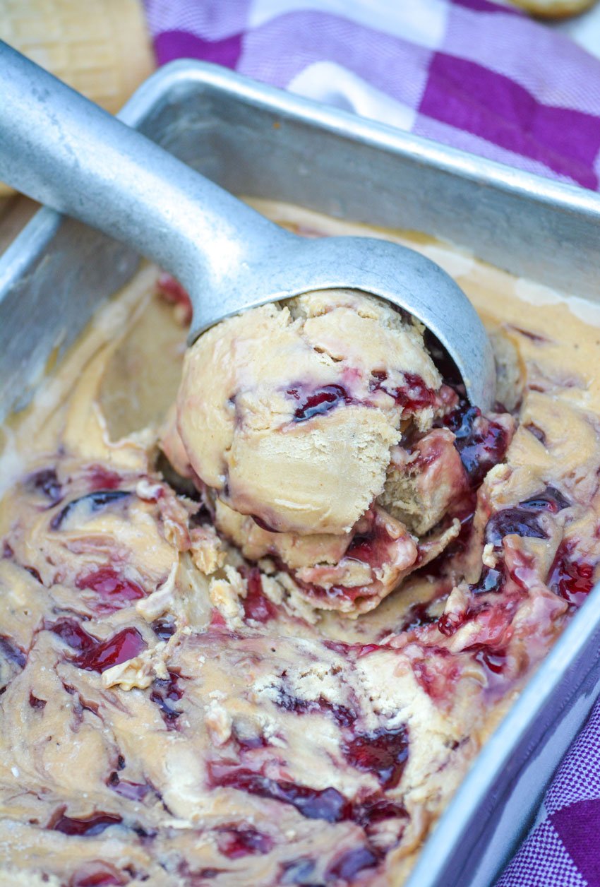 3 ingredient peanut butter and jelly ice cream being scooped by a silver ice cream scoop from a metal loaf pan