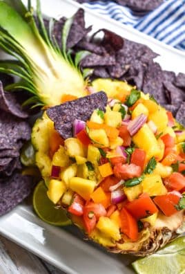 a blue corn tortilla chip sticking out of a pineapple bowl filled with pineapple mango salsa