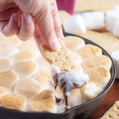 a hand holding a graham cracker dipped in easy skillet s'mores dip