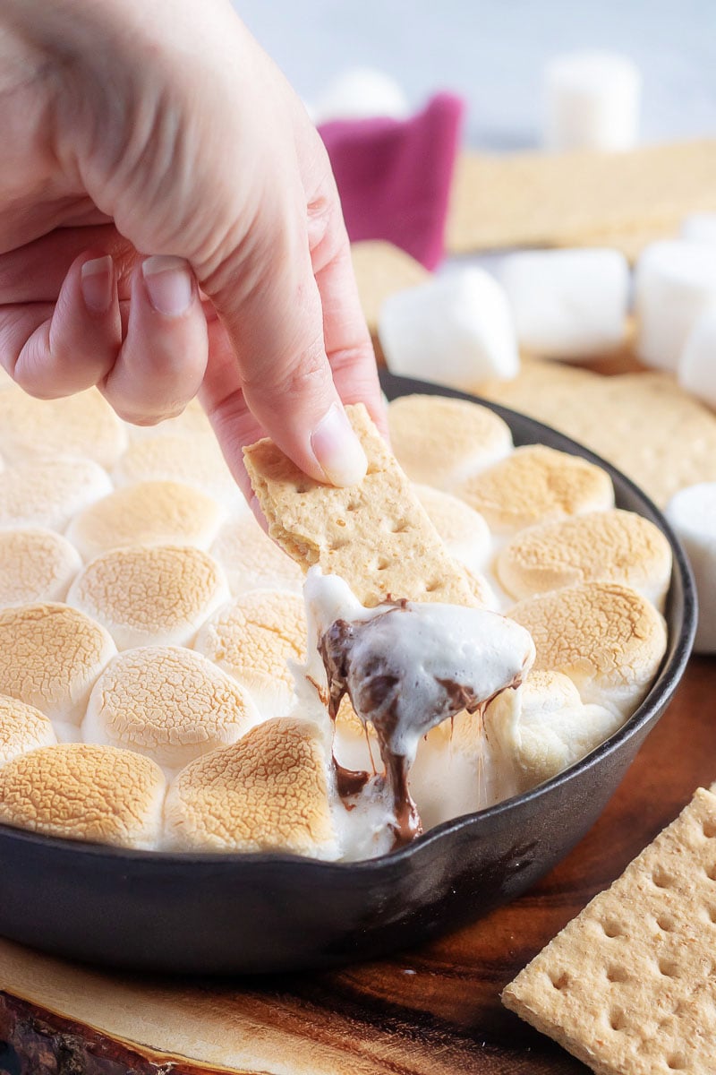 a hand holding a graham cracker dipped in easy skillet s'mores dip