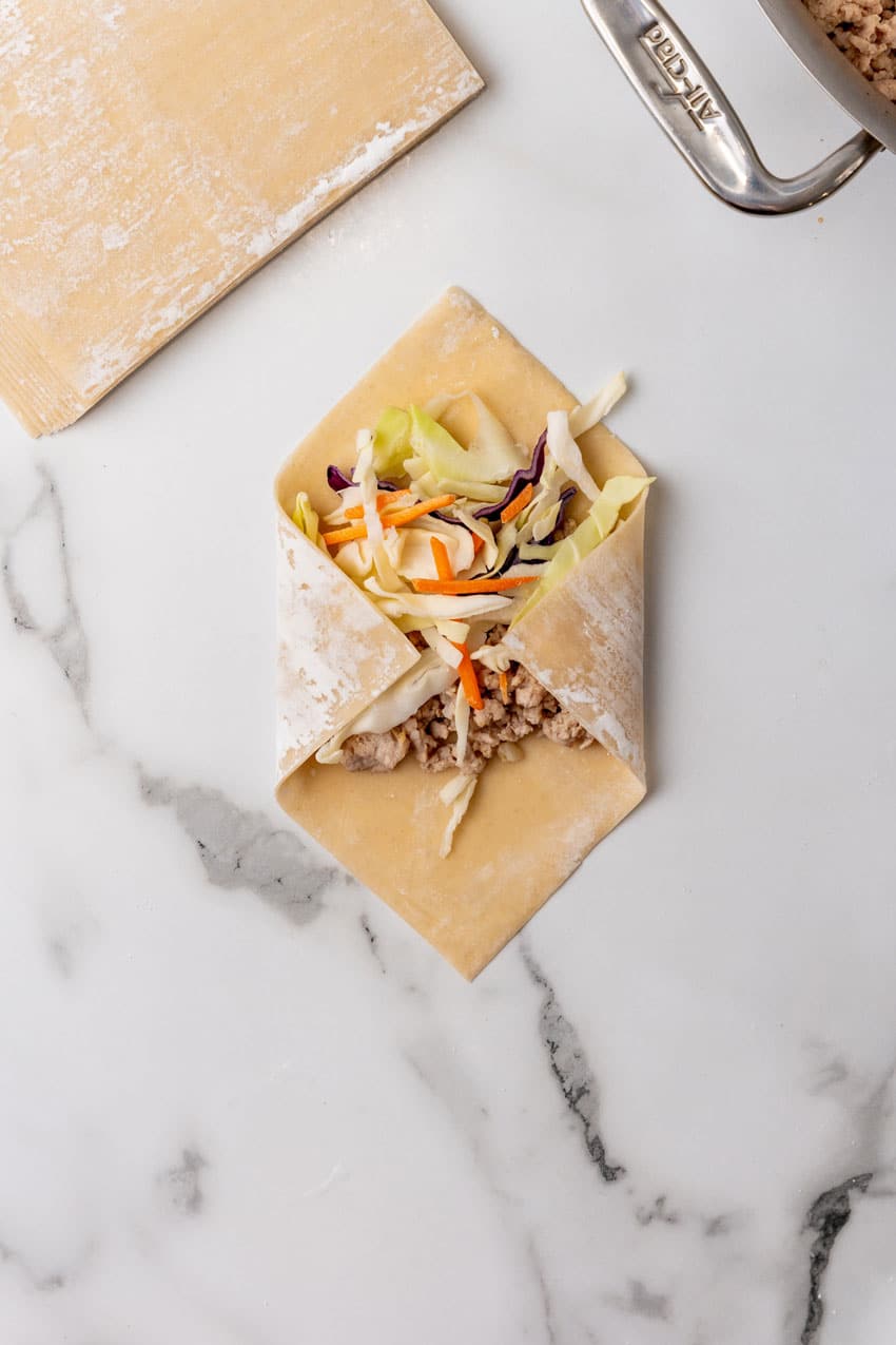 ground pork and shredded cabbage in the middle of an egg roll wrapper with the sides folded over the filling