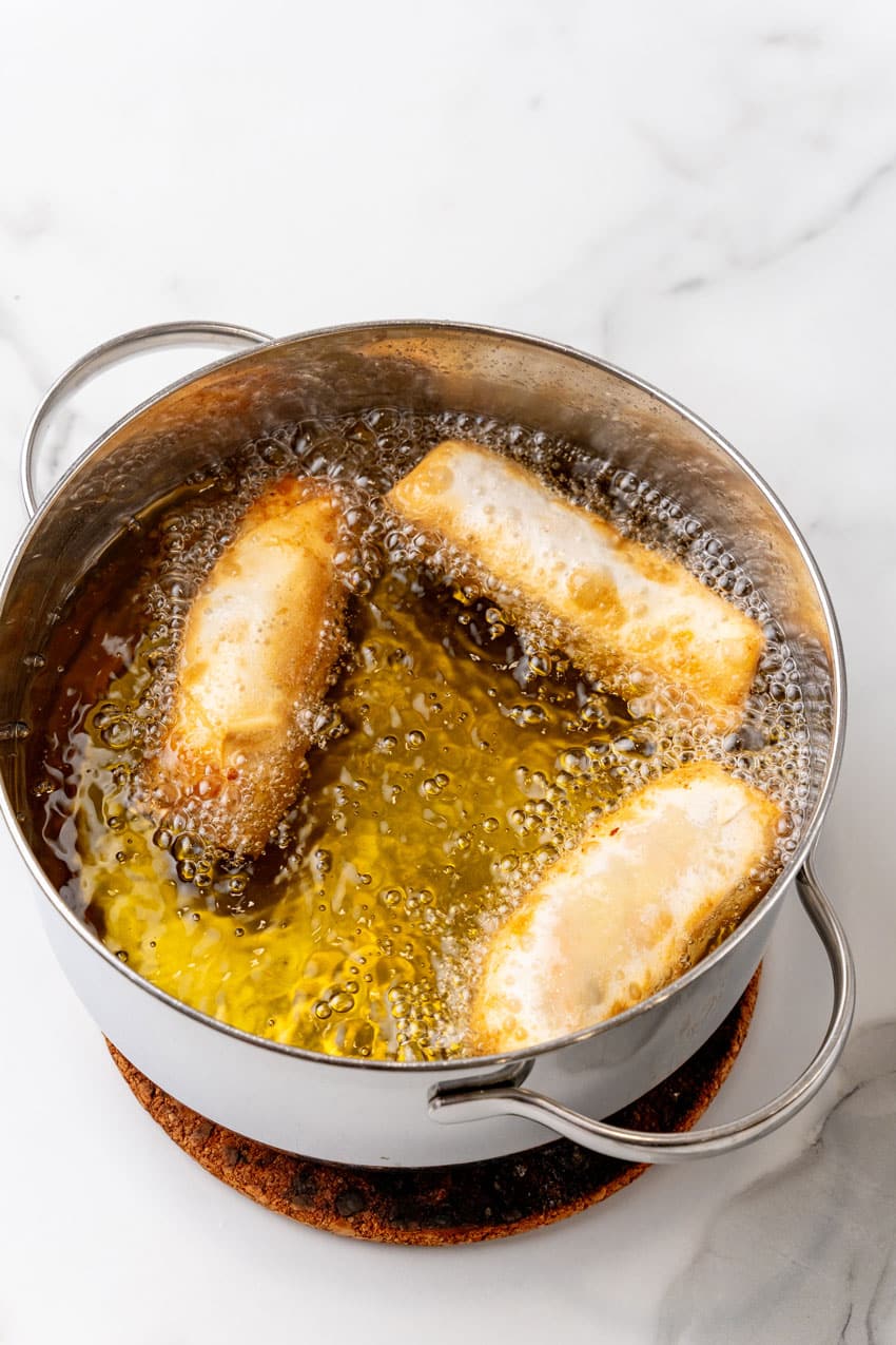 homemade pork egg rolls frying in a pot of hot oil