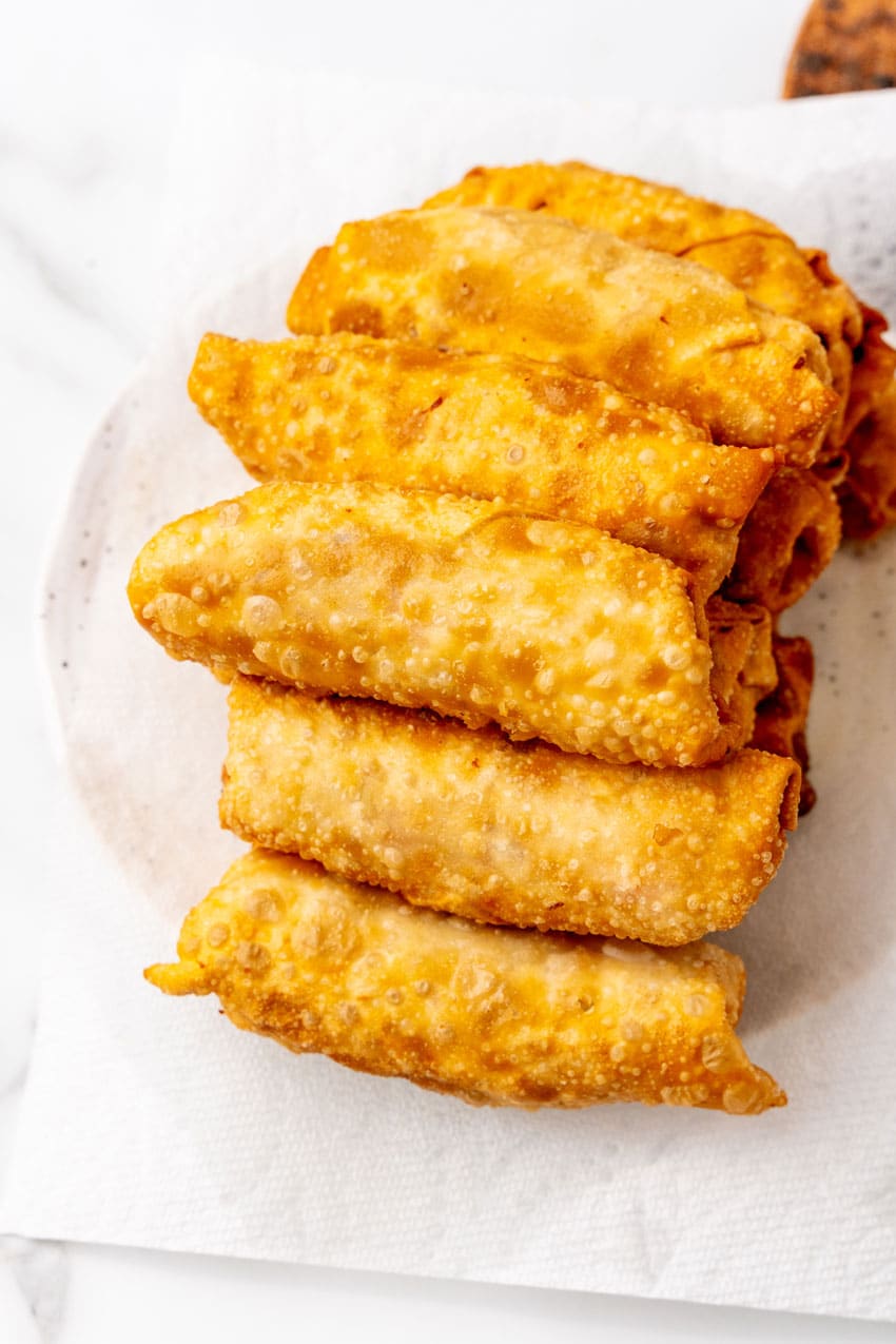 a pile of freshly fried homemade pork egg rolls draining on a paper towel lined plate