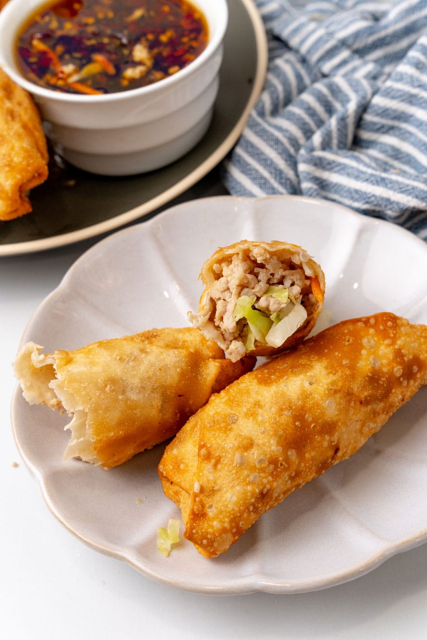 an opened egg roll revealing the filling inside resting on a small white appetizer plate