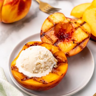 a grilled peach topped with vanilla ice cream on a white dessert plate
