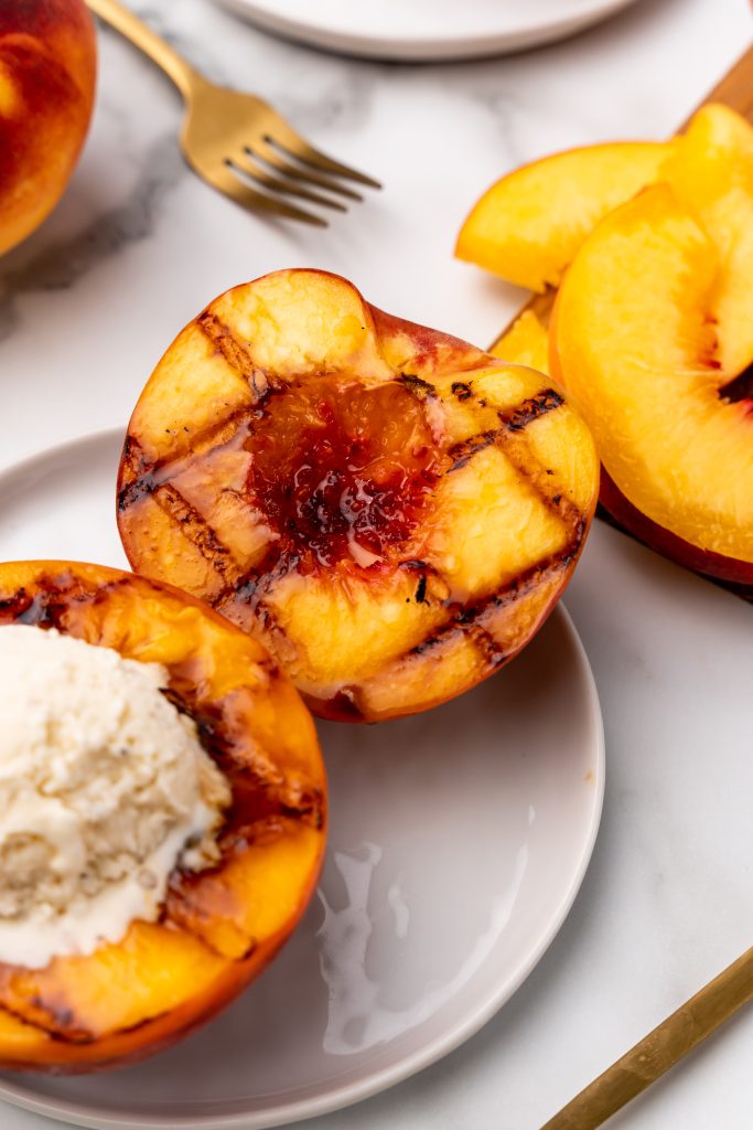 grilled peaches topped with vanilla ice cream on a small white dessert plate