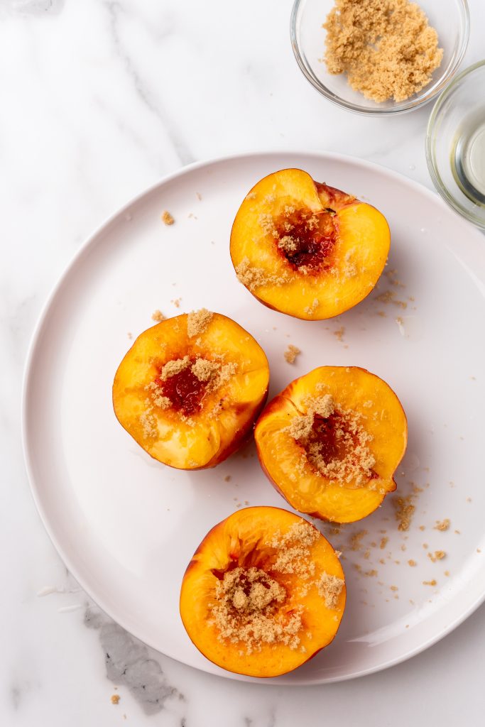 four oil brushed pitted peach halves sprinkled with brown sugar on a white plate
