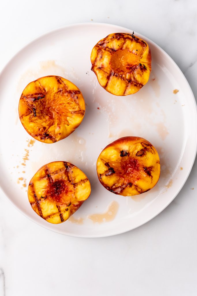 juicy grilled peach halves on a large white plate