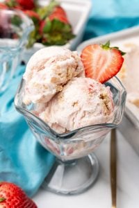 scoops of strawberry ice cream in a glass ice cream dish with a halved strawberry on the side for garnish