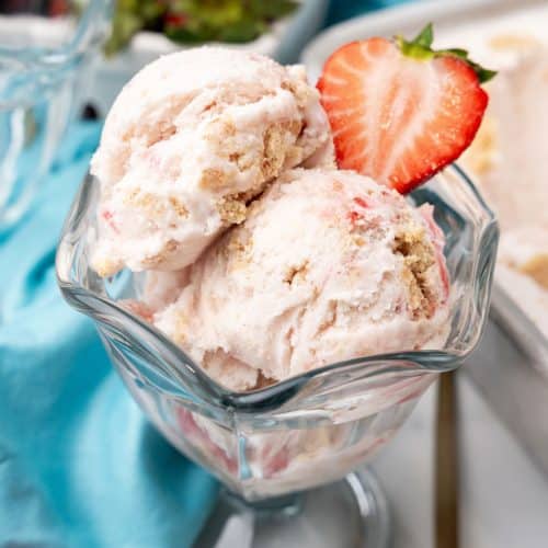 scoops of strawberry ice cream in a glass ice cream dish with a halved strawberry on the side for garnish