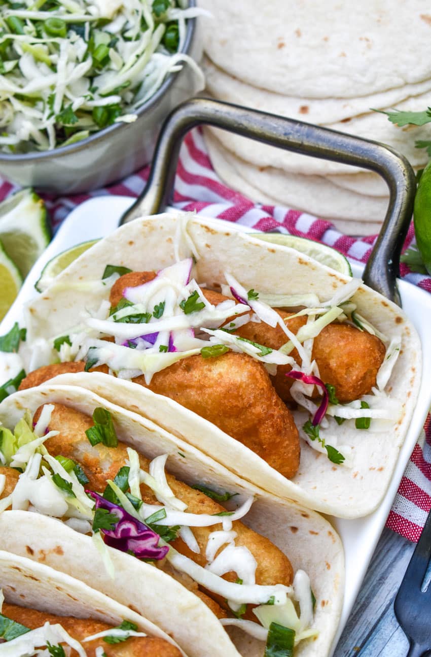 beer battered fish tacos arranged in a row on a white serving platter