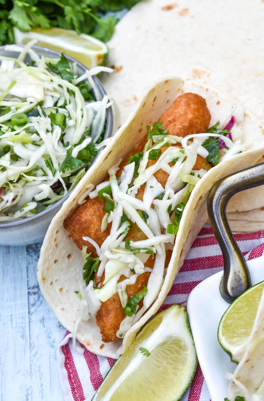 beer battered fish tacos arranged in a row on a white serving platter