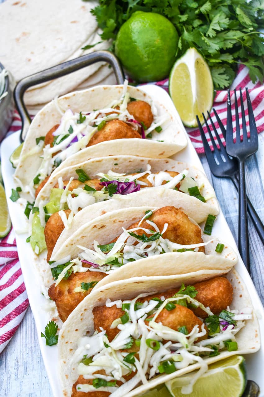 beer battered fish tacos arranged in a row on a white serving platter