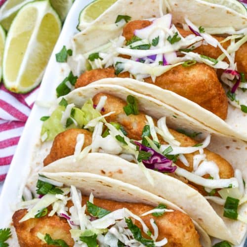 beer battered fish tacos arranged in a row on a white serving platter