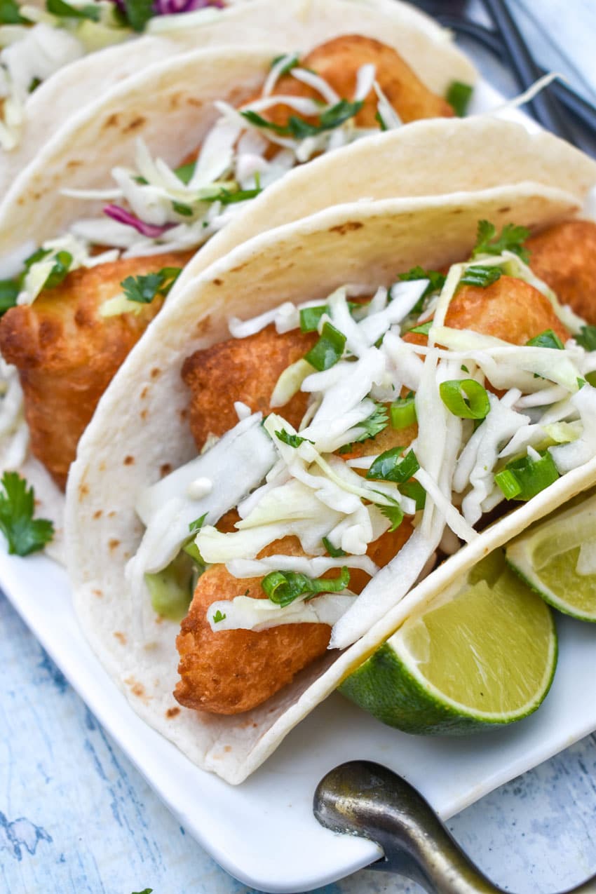 beer battered fish tacos arranged in a row on a white serving platter