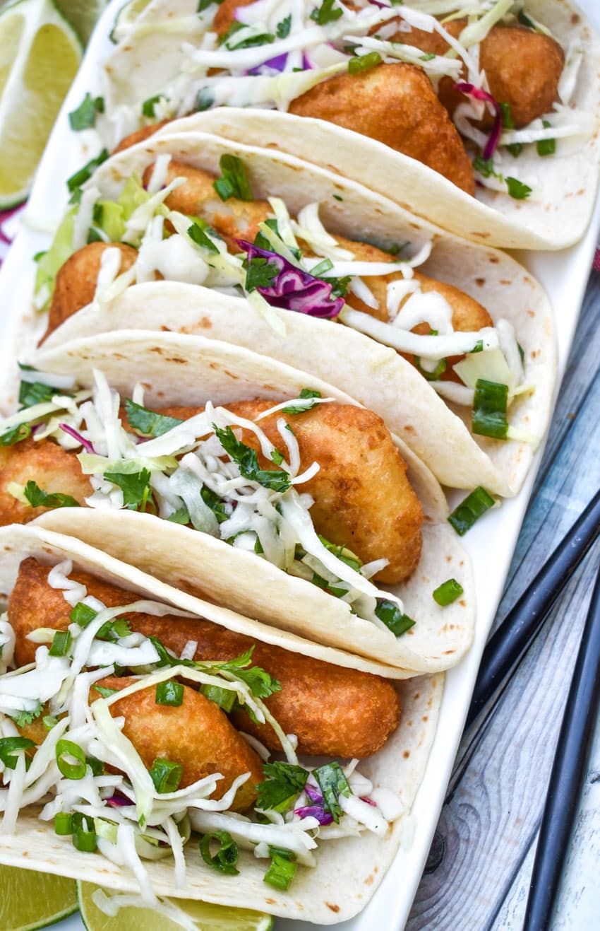 beer battered fish tacos arranged in a row on a white serving platter