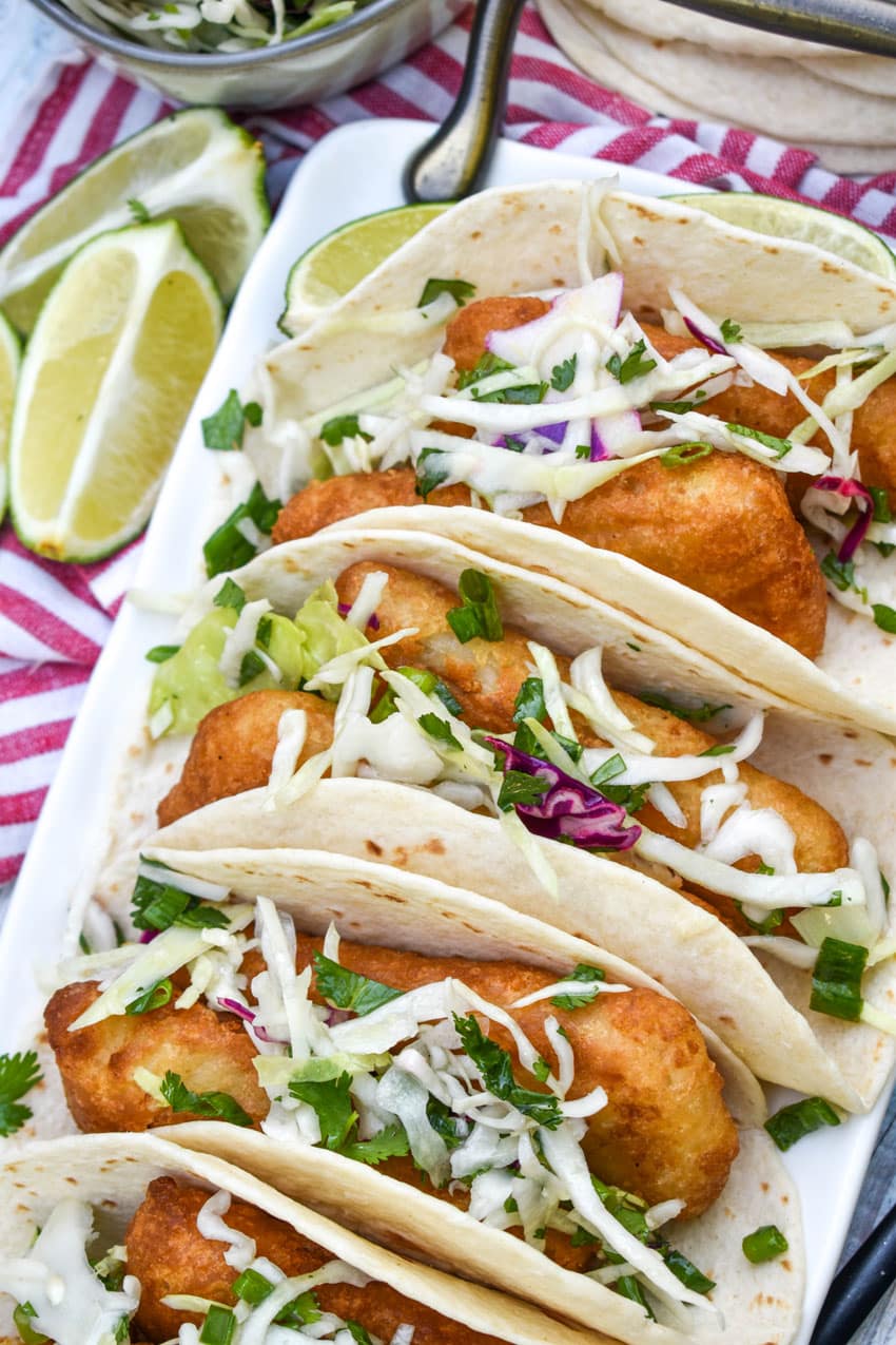 beer battered fish tacos arranged in a row on a white serving platter