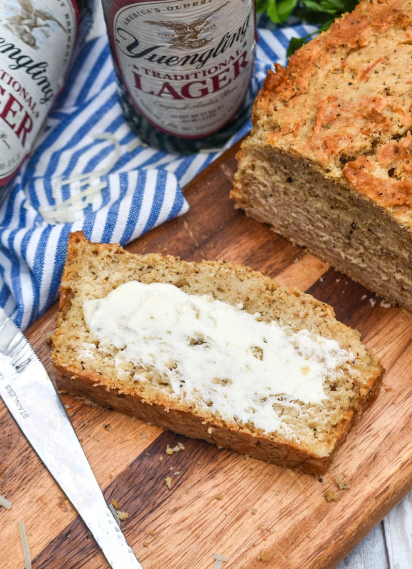 a slice of black pepper parmesan beer bread spread with butter resting on a wooden cutting board
