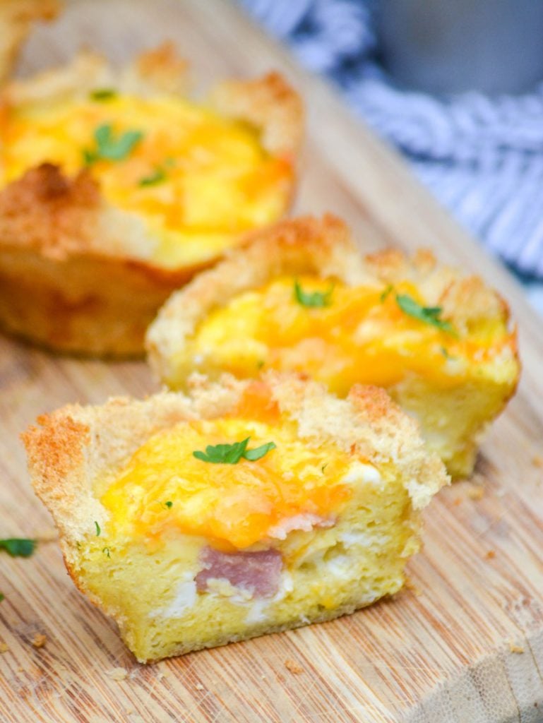 Ham, Egg, & Cheese Toast Cups cut in half to reveal the ham and cheese center on a brown cutting board
