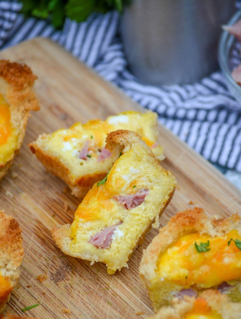 Ham, Egg, & Cheese Toast Cups cut in half and shown facing up to reveal the cheesy ham and egg insides on a cutting board