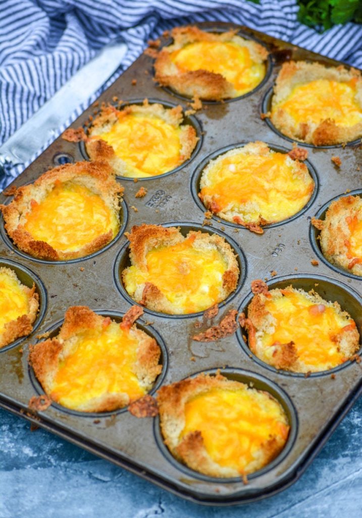 Ham, Egg, & Cheese Toast Cups in the silver muffin tin they were cooked in on a blue background with a striped cloth napkin