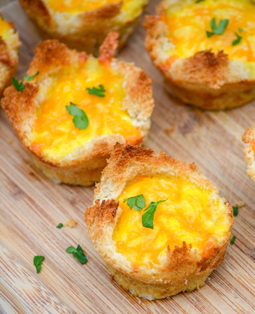 Ham, Egg, & Cheese Toast Cups on a brown cutting board and topped with fresh herbs